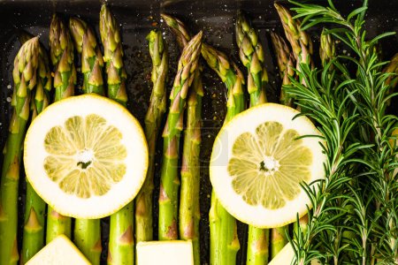 Photo for Fresh green asparagus, sliced lemon, and butter, fresh rosemary, and seasonig close up on baking sheet, ready to be baked, flat lay - Royalty Free Image