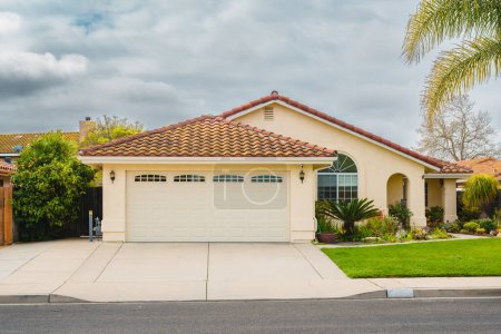 Beautiful houses with nicely landscaped front the yard in small town in California. Architecture, ornamental plants and flowers, palm trees, and cloudy sky in the background