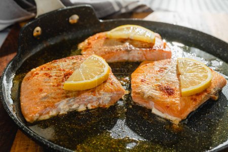 Photo for Salmon slices fried with seasoning, smoked paprika, and lemon slices, close-up on a frying pan - Royalty Free Image