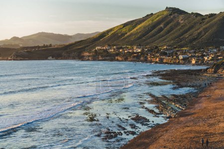Pismo beach cliffs, wide sandy beach at low tide, green hills, and silhouette of a town in the background at sunset, California Central Coast