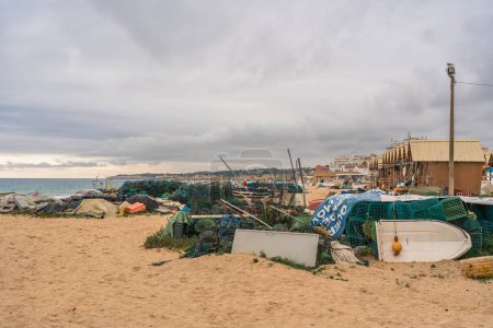 Photo for Fishing gear and boats scattered on a sandy beach under a cloudy sky. Algarve, Portugal, January 3, 2024 - Royalty Free Image