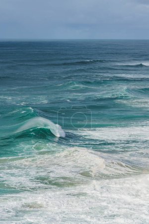 A magnificent wave curls with frothy white foam at Nazare, known for its big wave surfing.