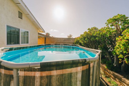 Foto de Patio trasero con una piscina sobre el suelo y exuberantes plantas verdes en un día soleado. - Imagen libre de derechos