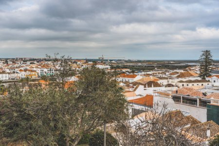 Blick auf Tavira, Portugal, mit einer Mischung aus traditioneller und moderner Architektur, mit orangefarbenen Ziegeldächern und Küstenlandschaft.