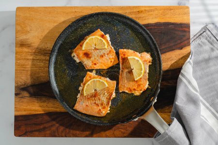 Photo for Fried salmon close-up on a frying pan on a wooden serving board on the kitchen table, flat lay - Royalty Free Image