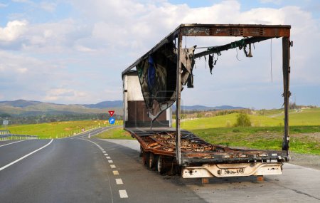 Image of a  burnt-out truck on the side of the road. The whole van burned down, the cargo was lost. Risks of cargo transportation. Blue skies with clouds.                      