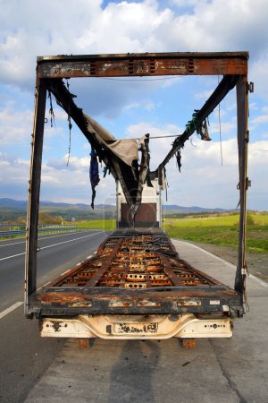Image of a  burnt-out truck on the side of the road. The whole van burned down, the cargo was lost. Risks of cargo transportation. Blue skies with clouds.                      