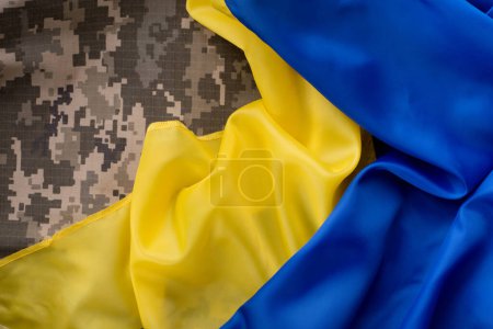 Yellow-blue flag of the state of Ukraine over military pixel camouflage fabric background.