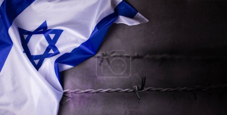 Photo for Holocaust Remembrance Day. Yom HaShoah. Official flag of Israel on a dark grey background in composition with barbed wire. Memorial Day for Jewish people. - Royalty Free Image