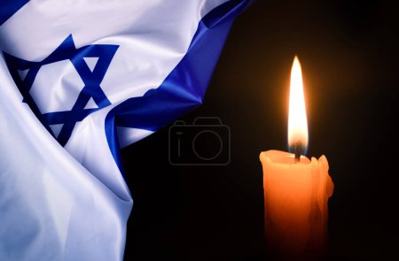 Photo for Holocaust Remembrance Day. Yom HaShoah. Bright Burning Candle and the official flag of Israel on a dark grey background. Memorial Day for Jewish people. - Royalty Free Image