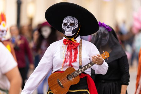 Téléchargez les photos : Matamoros, Tamaulipas, Mexique - novembre 1, 2022 : Dia de los Muertos Parade, Female dress up as mariachi wearing a skull mask and playing a small guitar - en image libre de droit