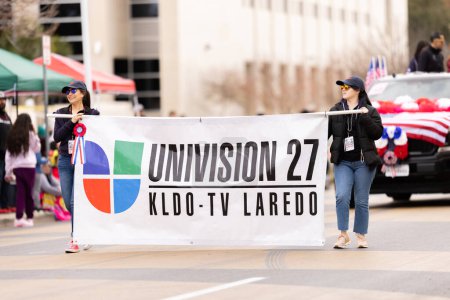 Foto de Laredo, Texas, Estados Unidos - 19 de febrero de 2022: Desfile de cumpleaños de Anheuser-Busch Washingtons, mujeres con pancarta promocionando Univision 27 KLDO TV Laredo - Imagen libre de derechos