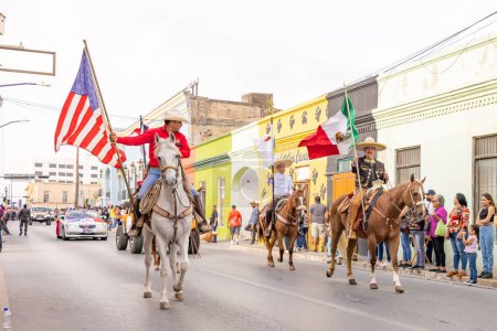 Foto de Matamoros, Tamaulipas, México - 25 de febrero de 2023: Desfile de Fiestas Mexicanas, Hombres a caballo portando la Bandera Mexicana y Americana - Imagen libre de derechos