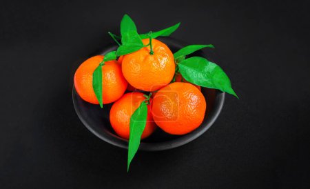 Téléchargez les photos : Oranges mandarines fraîches ou mandarines avec des feuilles sur fond noir. Copyspace. Mandarines fraîches cueillies Vue du dessus - en image libre de droit
