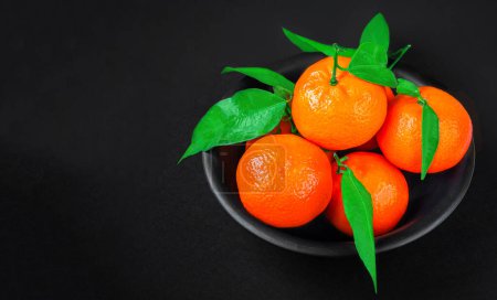 Téléchargez les photos : Oranges mandarines fraîches ou mandarines avec des feuilles sur fond noir. Copyspace. Mandarines fraîches cueillies Vue du dessus - en image libre de droit