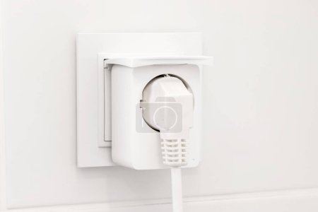 Foto de Enchufe eléctrico europeo blanco con enchufe inteligente insertado en él en moderno baño brillante con pared de azulejos blancos - Imagen libre de derechos