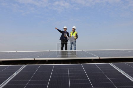 Téléchargez les photos : Ingénieur solaire et technicien discutant du dessin sur le toit de l'usine, Énergie solaire verte de renouvellement, Ingénieur et homme d'affaires travaillant sur place au toit solaire, Progressiste avec le projet solaire - en image libre de droit