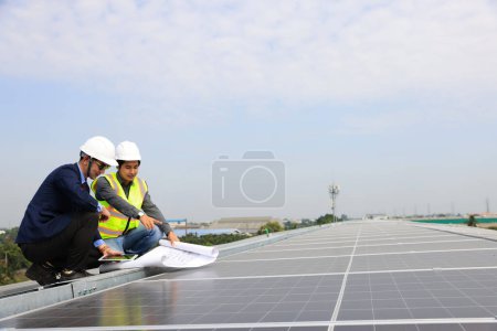 Téléchargez les photos : Ingénieur solaire et technicien discutant du dessin sur le toit de l'usine, Énergie solaire verte de renouvellement, Ingénieur et homme d'affaires travaillant sur place au toit solaire, Progressiste avec le projet solaire - en image libre de droit