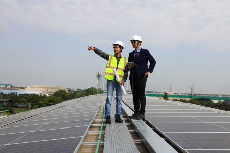 Foto de Solar engineer and technician discussing about blue print drawing on roof of factory, Solar green renewal energy ,Engineer and businessman working onsite at solar roof, Progressive with solar project - Imagen libre de derechos