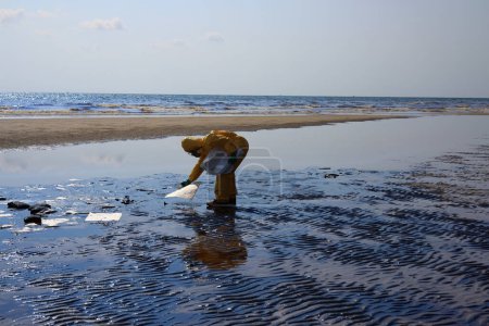 Téléchargez les photos : Une équipe professionnelle et un bénévole portant un EPI nettoient les déversements d'hydrocarbures sur la plage, la nappe d'hydrocarbures échouée sur une plage de sable - en image libre de droit