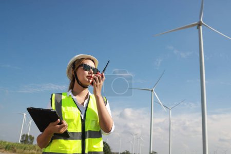 Photo for International Women's Day, you Asian woman with a green safety vest using a talkie at a windmill farm - Royalty Free Image
