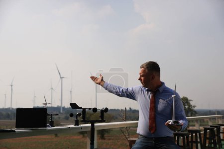 Photo for A senior male energy specialist is inspecting wind turbines on an ecological construction project using a wind speed measuring instrument at a windmill. - Royalty Free Image
