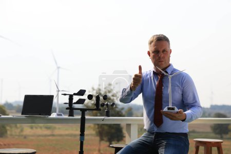 Foto de A senior male energy specialist is inspecting wind turbines on an ecological construction project using a wind speed measuring instrument at a windmill. - Imagen libre de derechos
