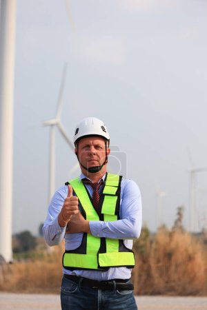 Photo for Senior Engineer smiling, arms crossed and looking at the camera at wind turbine background - Royalty Free Image