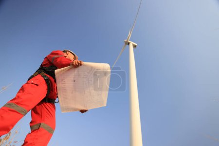  windmill engineer with red safety uniform hold drawing work at front of wind turbine farm 
