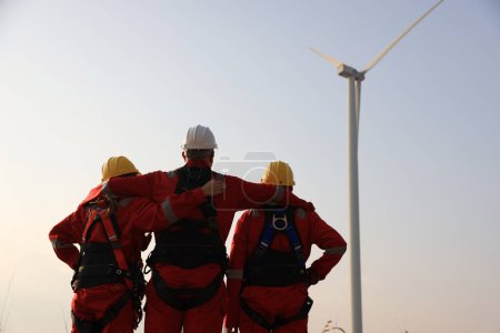  Equipo de ingenieros de molino de viento retrato con uniforme de trabajo rojo con sombrero duro de seguridad y arnés de trabajo en la granja de aerogeneradores 