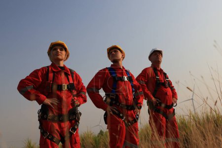 Equipo de ingenieros de molino de viento retrato con uniforme de trabajo rojo con sombrero duro de seguridad y arnés de trabajo en la granja de aerogeneradores 