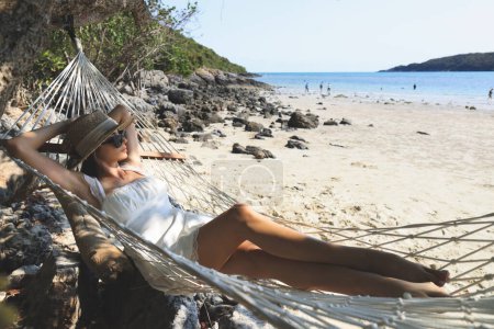 Porträt einer charmanten jungen Asiatin mit Sonnenbrille und glücklichem Lächeln Freizeit auf einer Hängematte Schaukel am Strand Meer und Meer mit blauem Himmel und weißen Wolken für den Urlaub