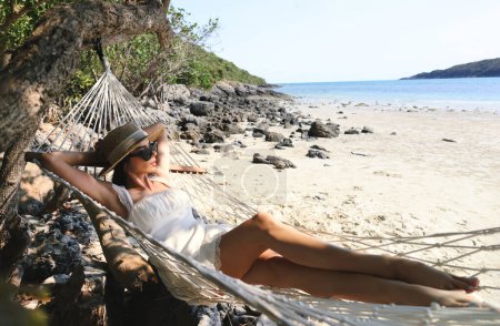 Portrait d'une charmante jeune femme asiatique avec un verre de soleil et un sourire heureux loisirs sur une balançoire hamac autour de la plage mer et océan avec ciel bleu et nuages blancs pour les vacances