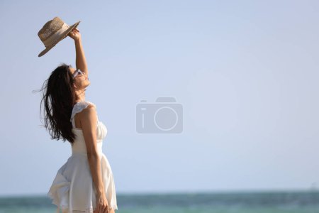 Téléchargez les photos : Joyeux belle femme avec robe décontractée blanche marcher avec pieds nus pour se détendre sur la plage tropicale, vacances d'été et Voyage S'éloigner de tout cela et remplir l'énergie avant de venir au travail - en image libre de droit
