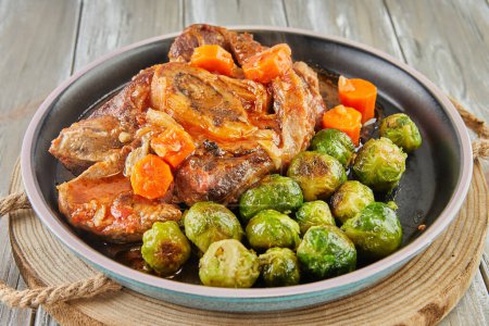 French recipe Brussels sprouts with ossobuco meat on black plate on wooden background.