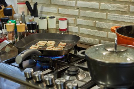Photo for Halloumi cheese is fried on ribbed pan over fire on gas stove. - Royalty Free Image