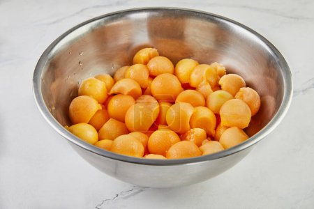 Téléchargez les photos : Boules de melon coupées avec une cuillère spéciale, dans un bol dans la cuisine. - en image libre de droit