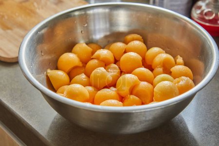 Téléchargez les photos : Boules de melon coupées avec une cuillère spéciale, dans un bol dans la cuisine. - en image libre de droit