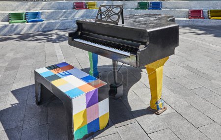 Foto de Piano negro en la plaza de la ciudad, bancos de colores alrededor. Concepto musical. - Imagen libre de derechos