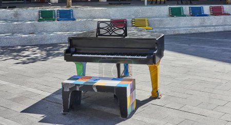 Foto de Piano negro en la plaza de la ciudad, bancos de colores alrededor. Concepto musical. - Imagen libre de derechos