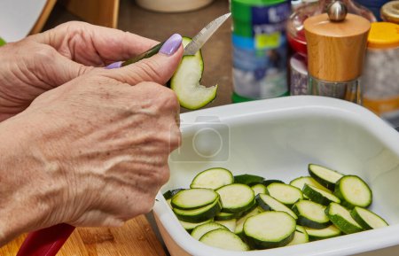 Photo for Close-up of a chef's hands expertly slicing fresh zucchini on a wooden cutting board in a bright modern kitchen. An experienced chef uses a sharp knife to prepare delicious food. - Royalty Free Image