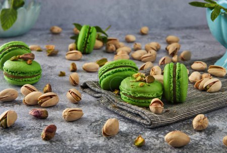 Delicious pistachio flavored macarons beautifully arranged on a vintage grey wooden background, garnished with fresh mint leaves. Perfect image for confectionery, dessert, or food blog content.