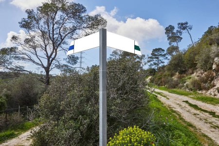 A blank trail signpost in a natural setting with two paths in the woods. Metal post with blank custom signs, gravel bed, trees. Left wide path, right narrow. Elevated view of signpost and paths.