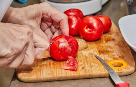 Close-up shot of a chef's hands expertly slicing fresh tomatoes on a wooden cutting board in a bright, modern kitchen. The skilled chef is using a sharp knife to prepare a delicious meal.