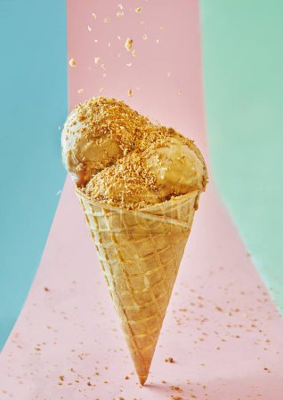A bright and tempting pecan ice cream cone with crushed nuts on a pink background for a refreshing and delicious treat. The image is well lit, with vibrant colors, adding to its appeal.