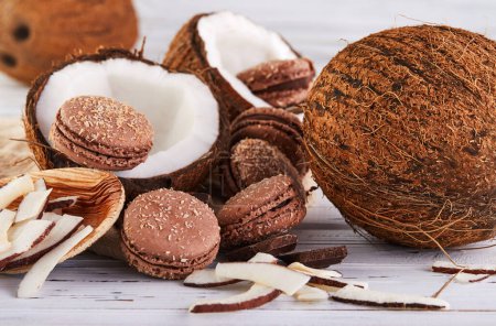 Téléchargez les photos : Macarons de noix de coco au chocolat et flocons de noix de coco sur une table avec une noix de coco en arrière-plan. L'image parfaite pour un blog alimentaire ou un site de recettes. - en image libre de droit