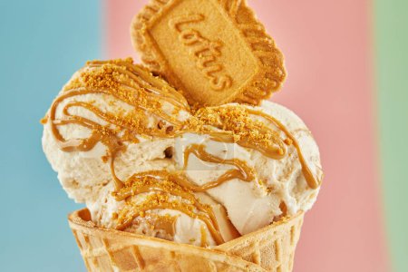 Delicious ice cream cone with a crispy biscuit on a colorful background. Generously topped with luscious caramel sauce for extra sweetness. Perfect for food-related content. Close up.