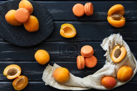 Délicieux macaron à la saveur d'abricot sur un fond sombre avec des abricots. Image idéale pour la cuisson, desserts ou contenu blog alimentaire.