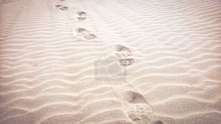 Téléchargez les photos : Empreintes de pas sur la plage avec un motif ondulé créé par le vent, fond de plage de sable chaud avec des bottes de combat empreintes de pieds avec vignette - en image libre de droit