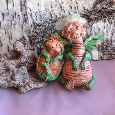 Two handmade dolls of green mama and baby family dragons with wings on birch bark background